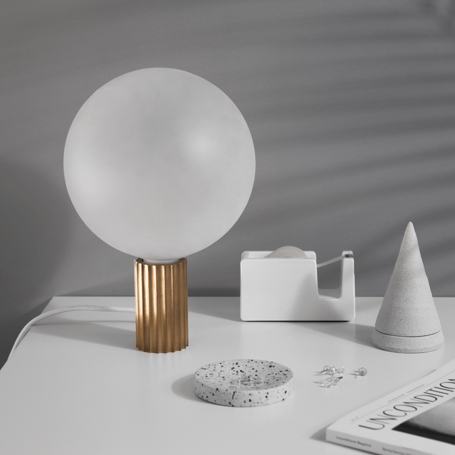 White globe table lamp on a ribbed brass-toned base beside small objects.