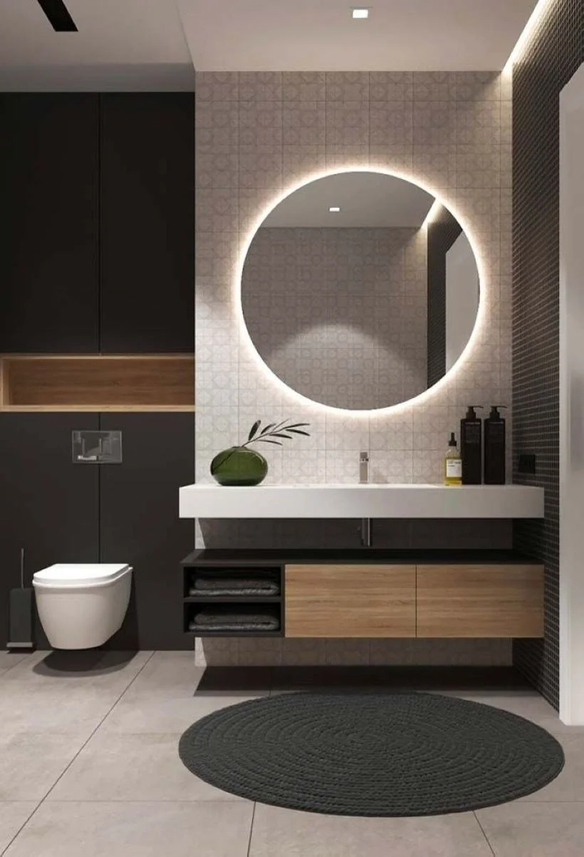 Bathroom vanity beneath a large illuminated round mirror.