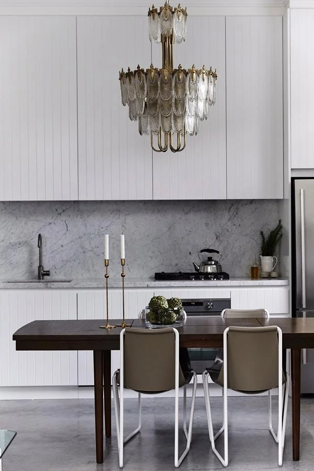 Crystal pendant above a dining table beside a pale kitchen.
