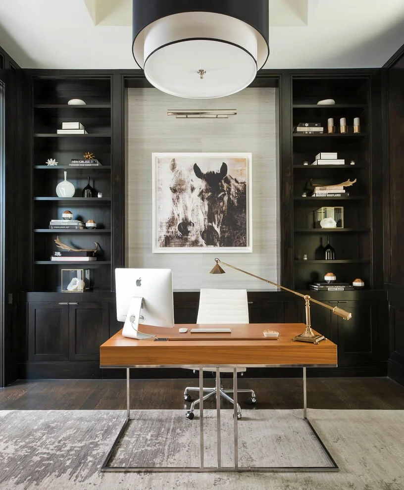 Study with dark shelving, a timber desk and a large circular ceiling light.
