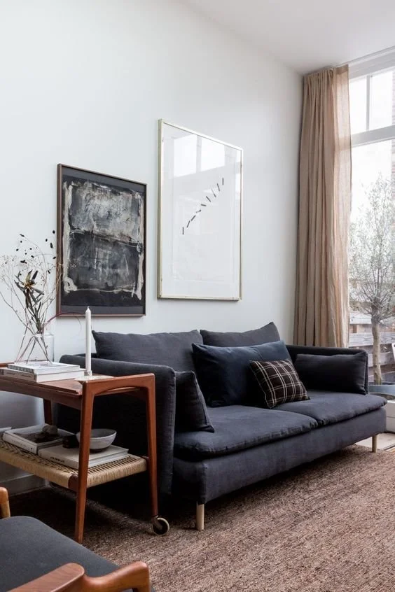 Dark sofa and timber furniture in a light room with tall curtains.