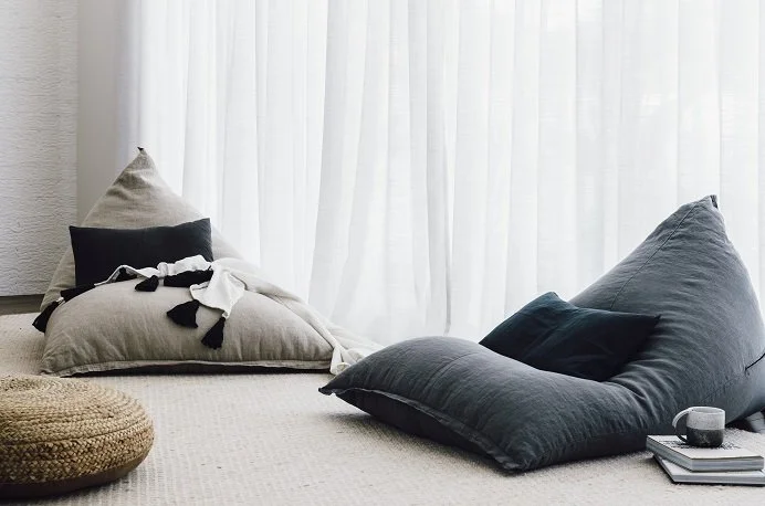 Soft upholstered floor cushions beside full-height sheer curtains.