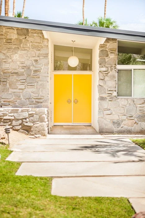 Stone house entrance with a vivid yellow door and stepping-stone path.