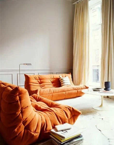 Orange upholstered sofa beside tall curtains in a softly lit living room.