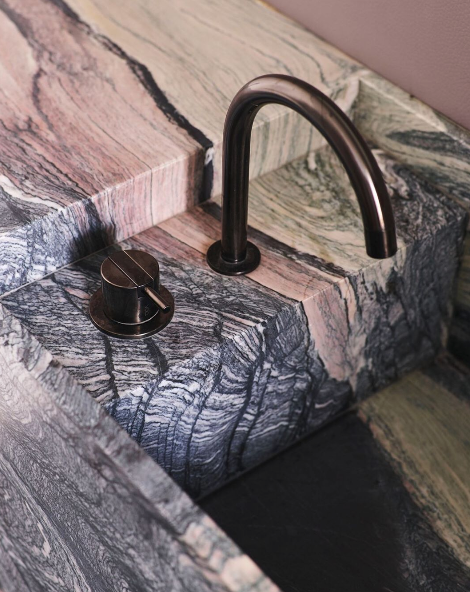 Veined stone sink with a dark curved tap integrated into the surrounding bench.