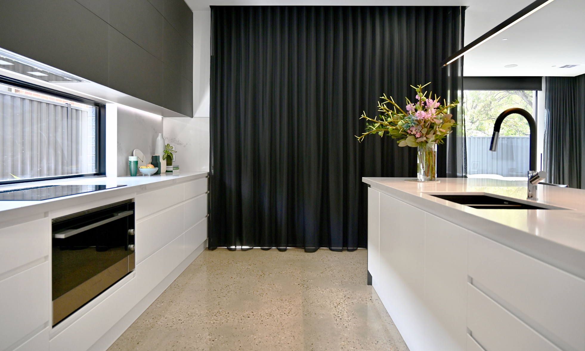 Contemporary kitchen with a pale island, black wall finishes and a long window.
