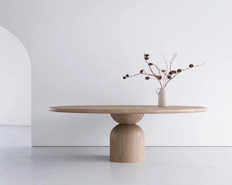 Sculptural round pale table with a rounded pedestal base and flowering branches.