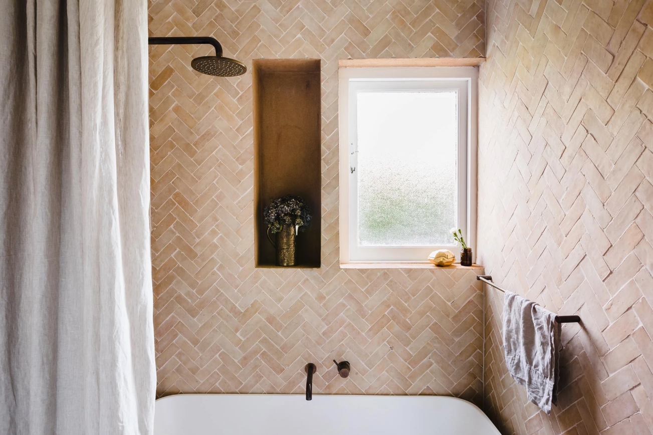 Bathroom with warm textured walls, a recessed shelf and a white bath.