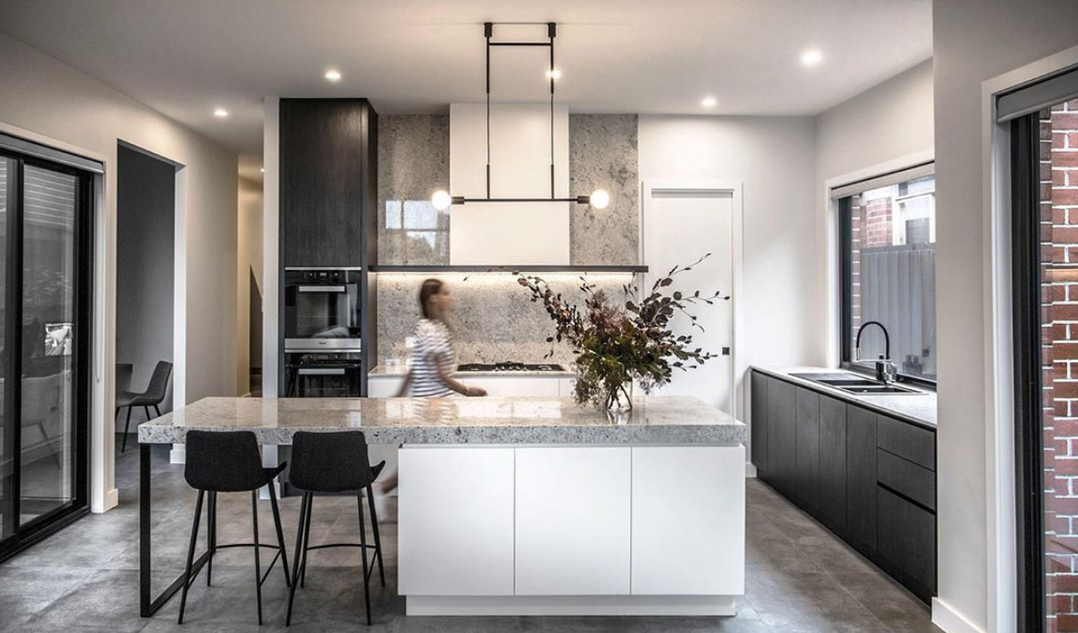 Kitchen island with seating between dark cabinetry and large windows.
