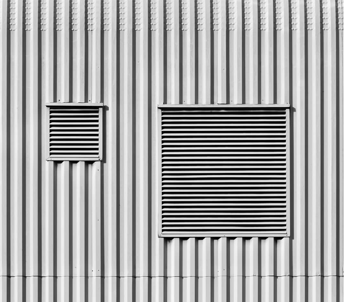 Vertical ribbed wall surface with two rectangular ventilation grilles.
