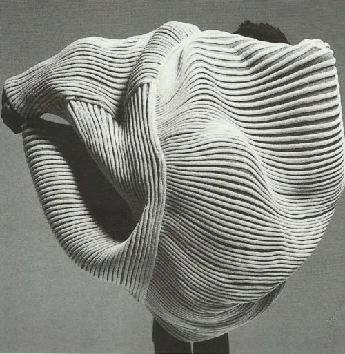 Pale sculptural object with closely layered wavy ridges.