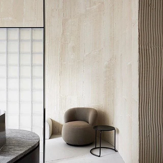 Minimal room with textured pale walls, a curved chair and dark side table.