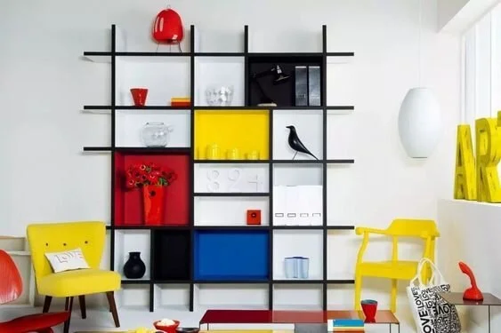 Black open shelving with red, yellow and blue panels beside yellow chairs.
