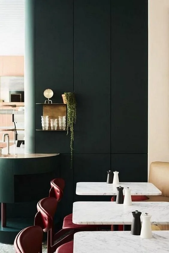 Deep green wall panelling behind a dining table with red and white chairs.