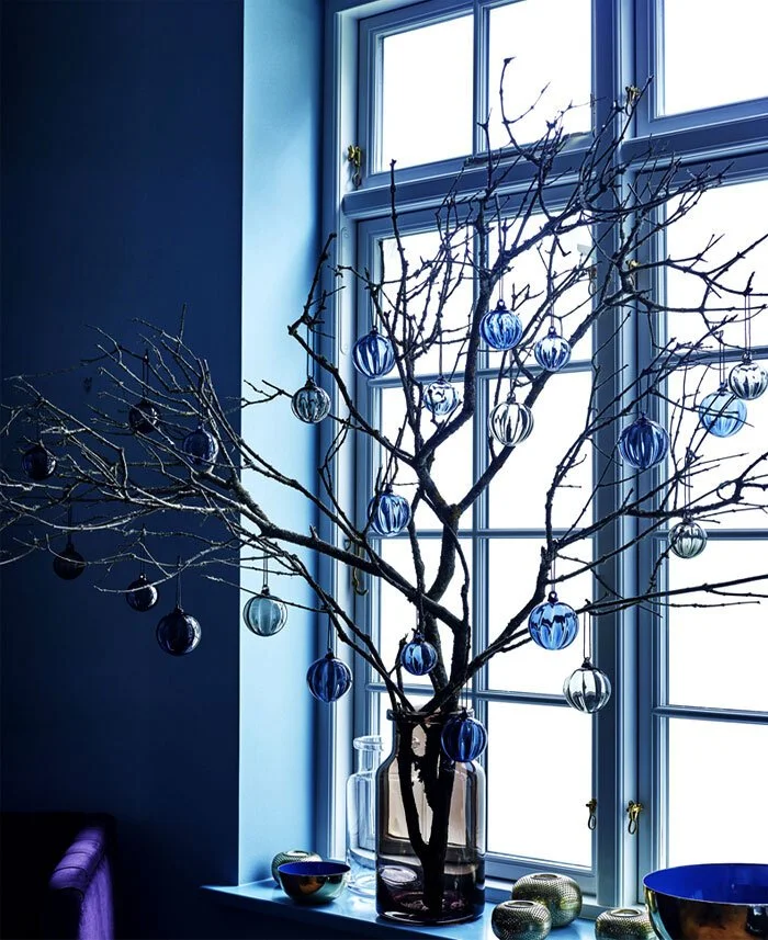 Bare decorative branches beside a window in a deep blue room.