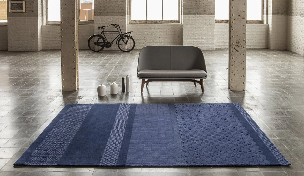 Large deep blue rug beneath a grey lounge chair in a light interior.
