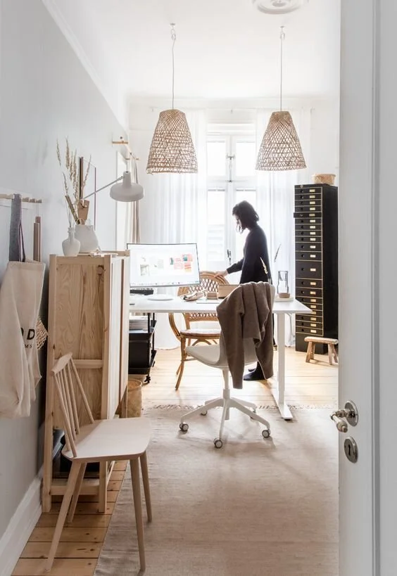 View through a doorway to a light home office with a desk and pendant lights.