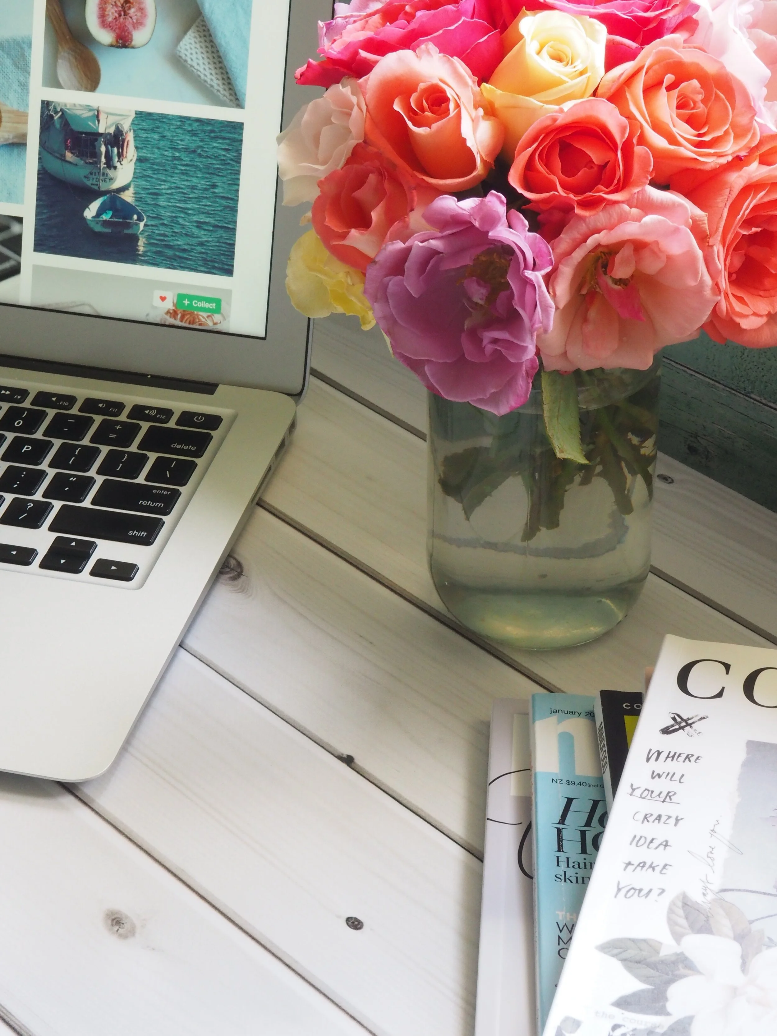 Laptop and books beside a vase of colourful flowers on a desk.