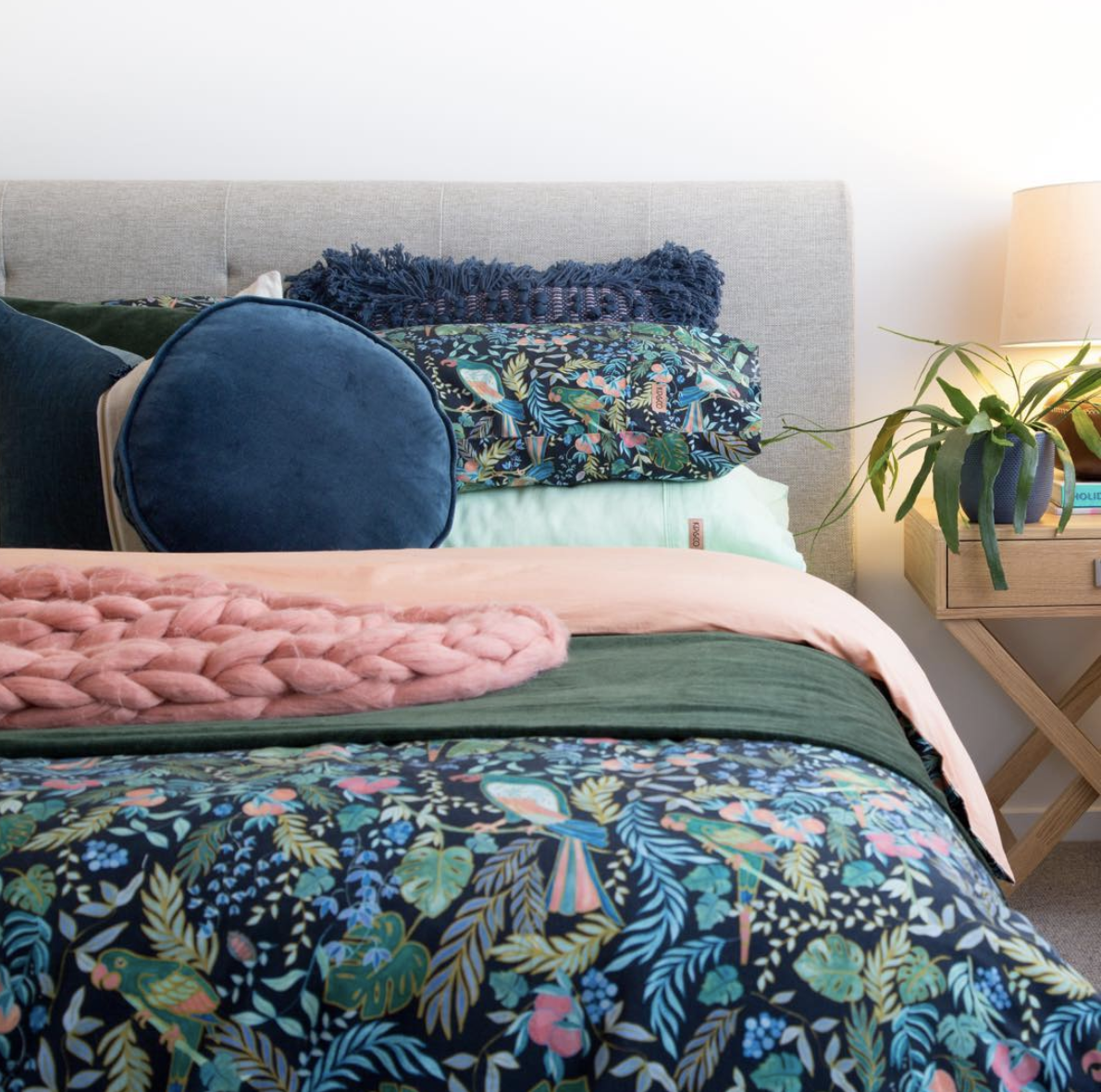 Colourful floral bedding with blue and pink cushions and a knitted throw.