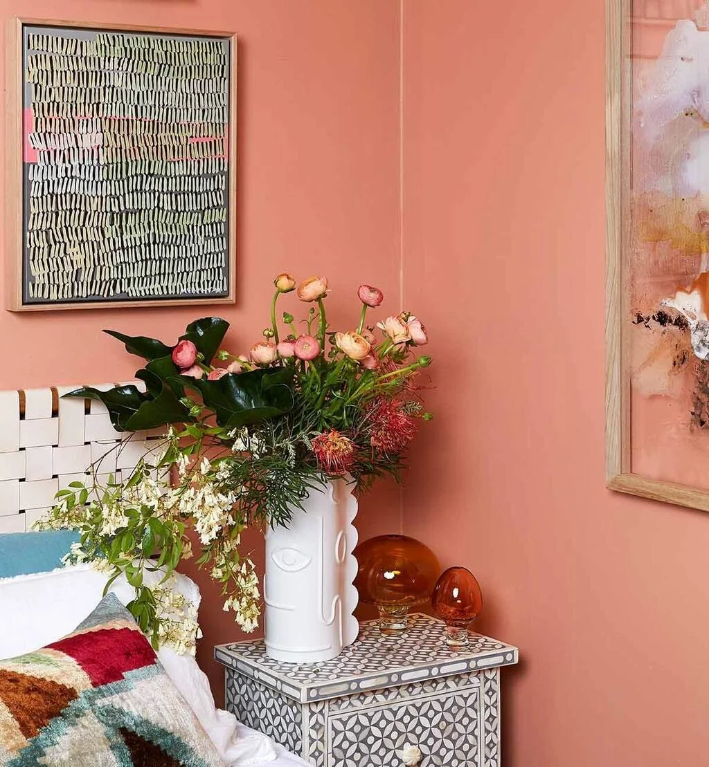 Coral-toned interior with framed artworks, flowers and a decorative side table.