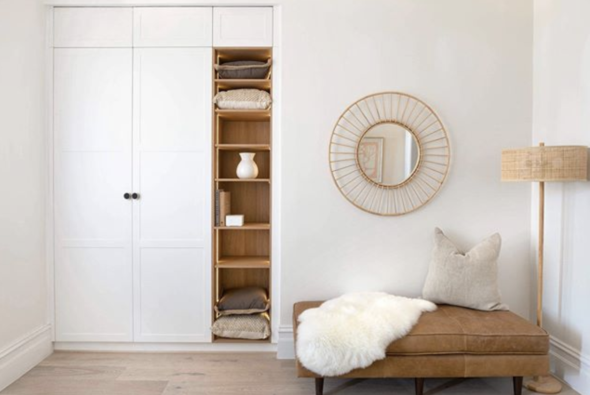 Pale wardrobe cabinetry with open timber shelving beside a cushioned bench.