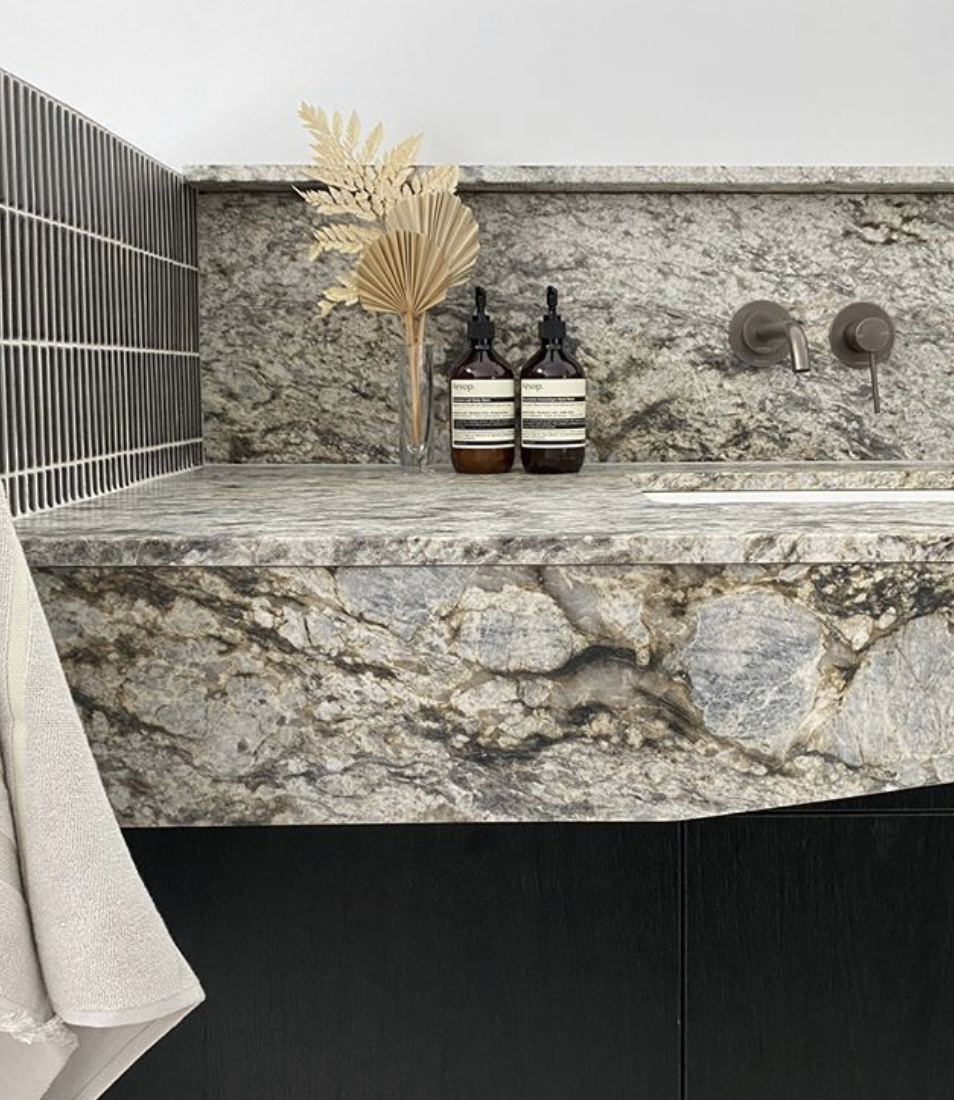 Veined stone vanity with dark cabinetry and bottles arranged beneath a tiled splashback.