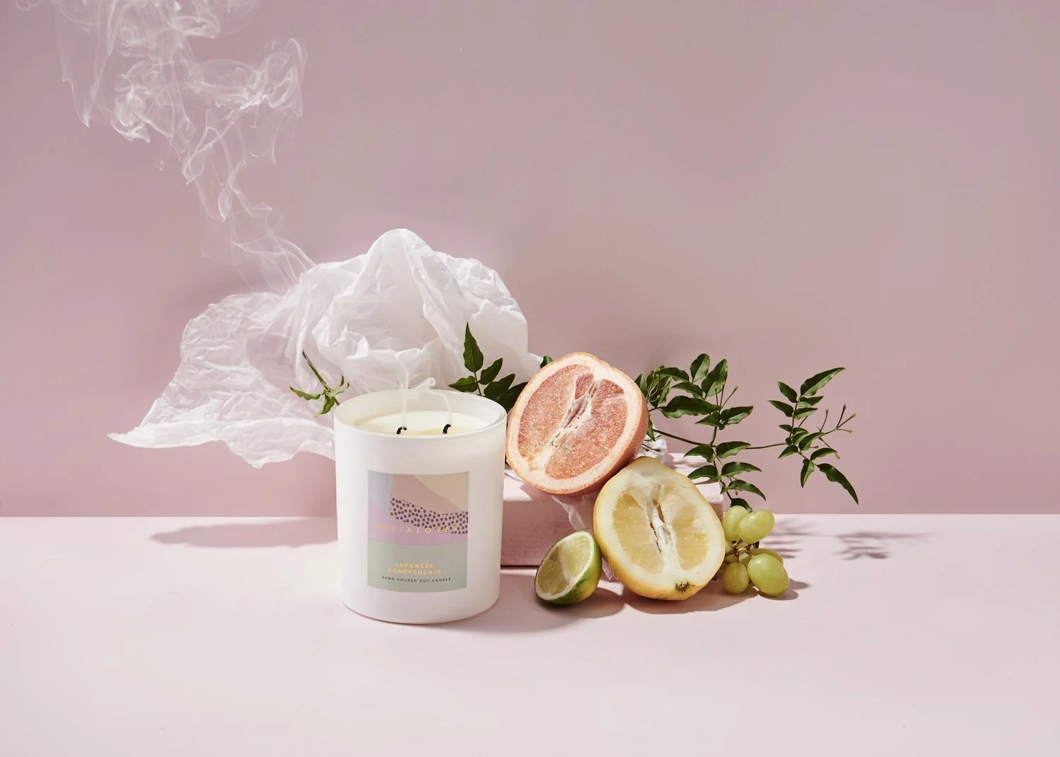 Scented candle with citrus slices and white flowers against a pink background.