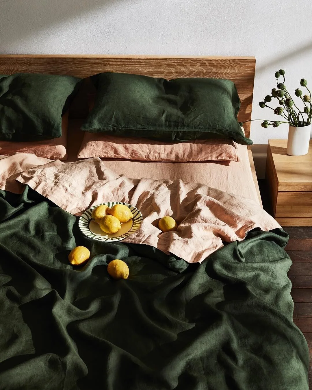 Layered green and pink bed linen with fruit and foliage arranged on the bed.