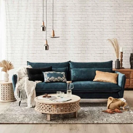 Deep teal sofa with layered cushions and a round woven coffee table.