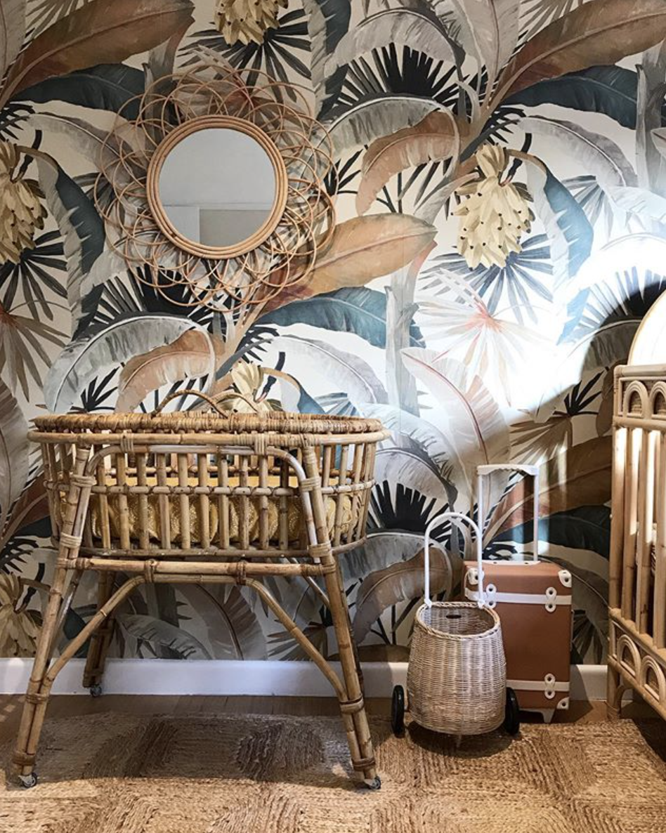 Botanical wallpaper behind woven furniture and a round mirror.