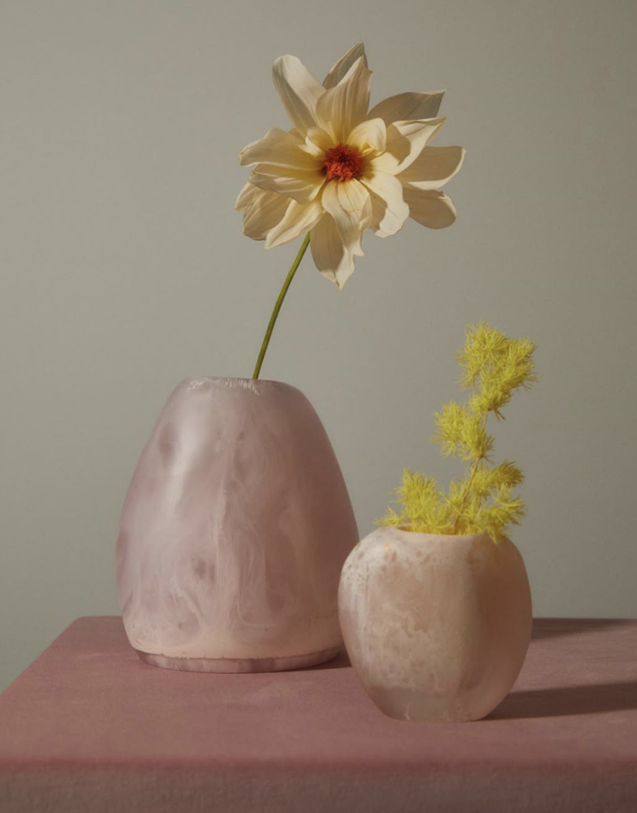 Pink-toned ceramic vases holding yellow flowers on a muted pink surface.