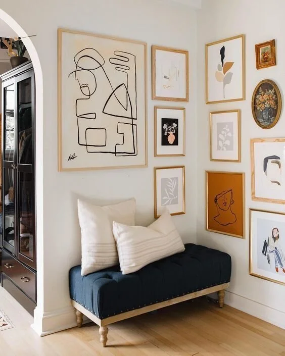 Gallery wall of varied framed artworks above a compact dark sofa.
