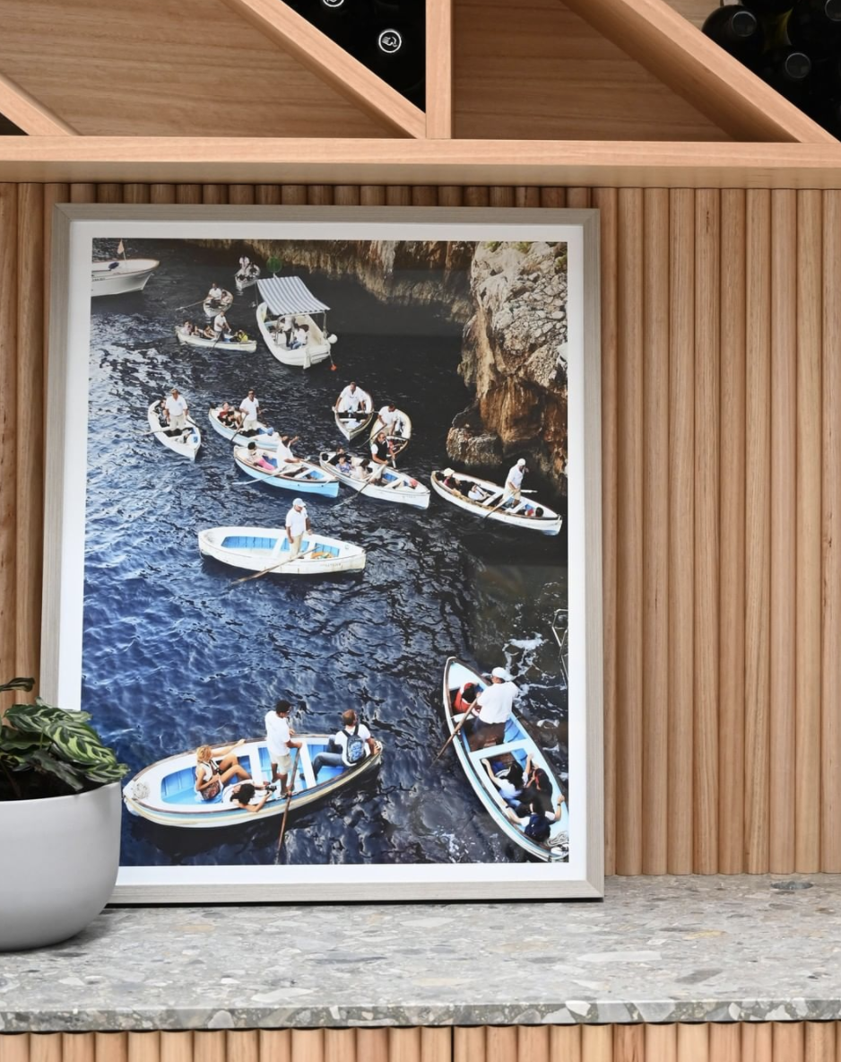 Framed photograph of boats against vertical timber panelling.
