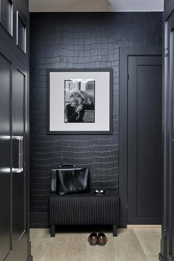 Dark textured wallpaper and framed art above a black upholstered seat.