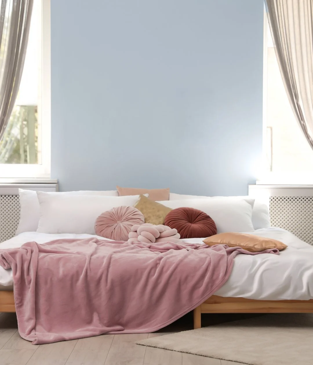 Bedroom with pale blue wall, pink linen and softly draped curtains.