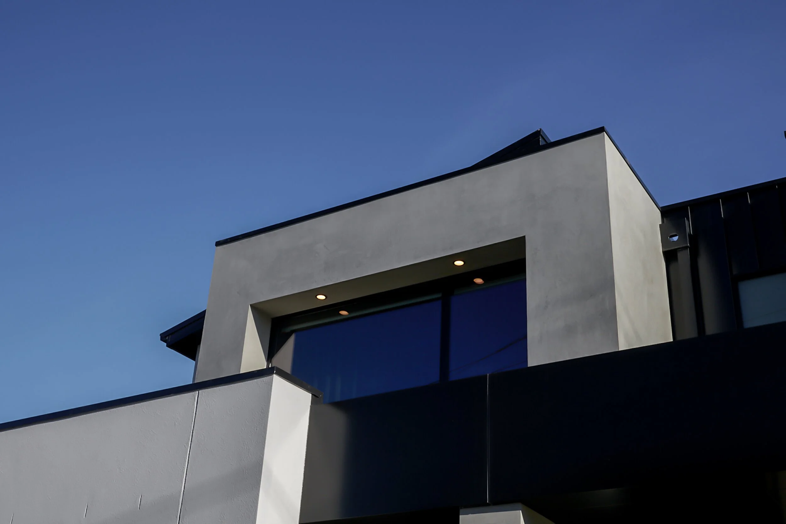 Contemporary house facade with angular grey forms beneath a blue sky.