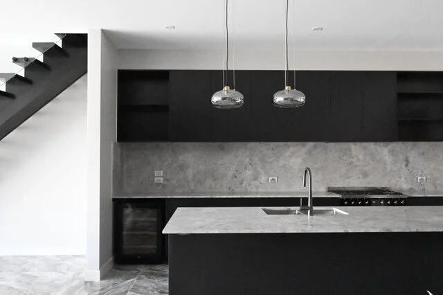 Dark kitchen cabinetry, a pale stone island and two glass pendant lights.