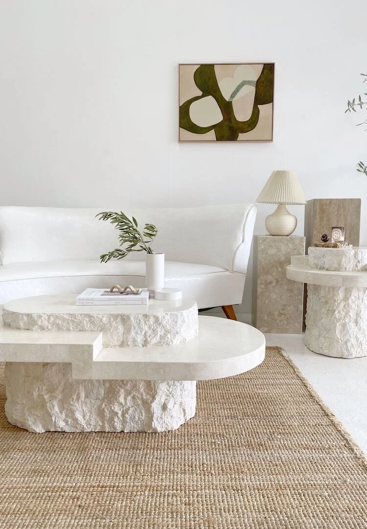 Pale living-room furnishings with a round stone coffee table and abstract art.