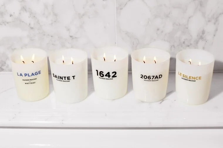 White candles with printed labels arranged on a pale stone surface.