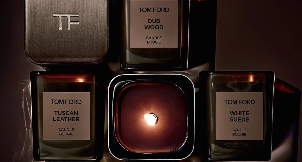 Dark square fragrance containers surrounding a lit candle.