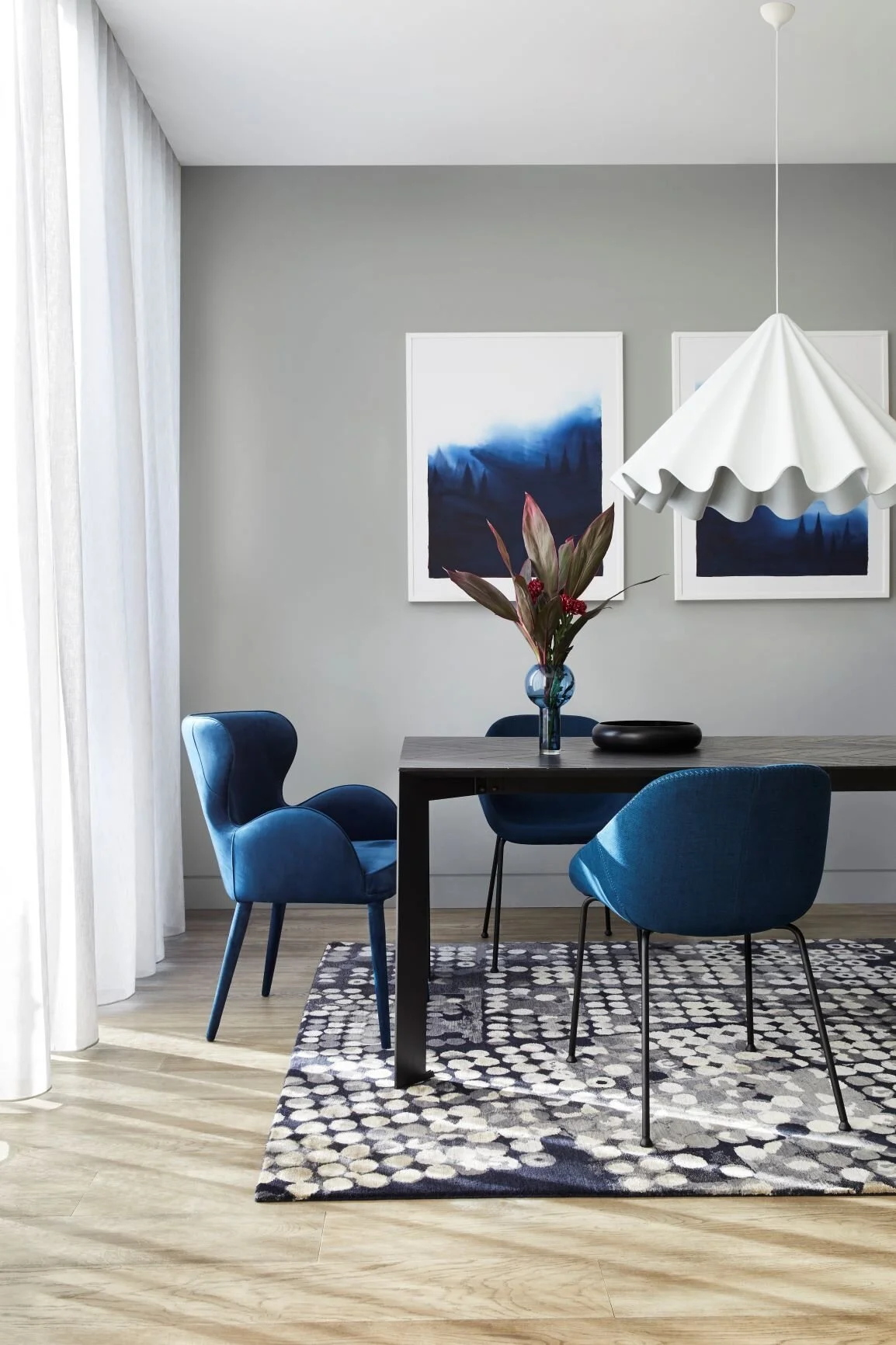 Blue dining chairs around a dark table beneath a sculptural white pendant.