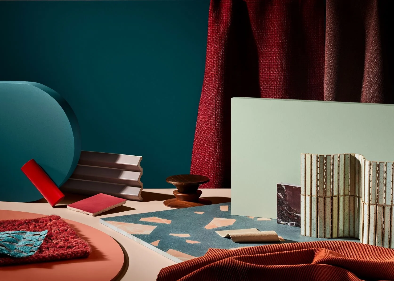 Deep teal and red colour composition with layered fabric and decorative objects.