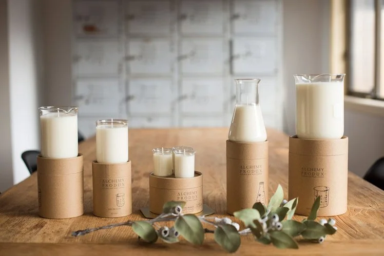 White candles raised on varied timber cylinders beside leafy branches.