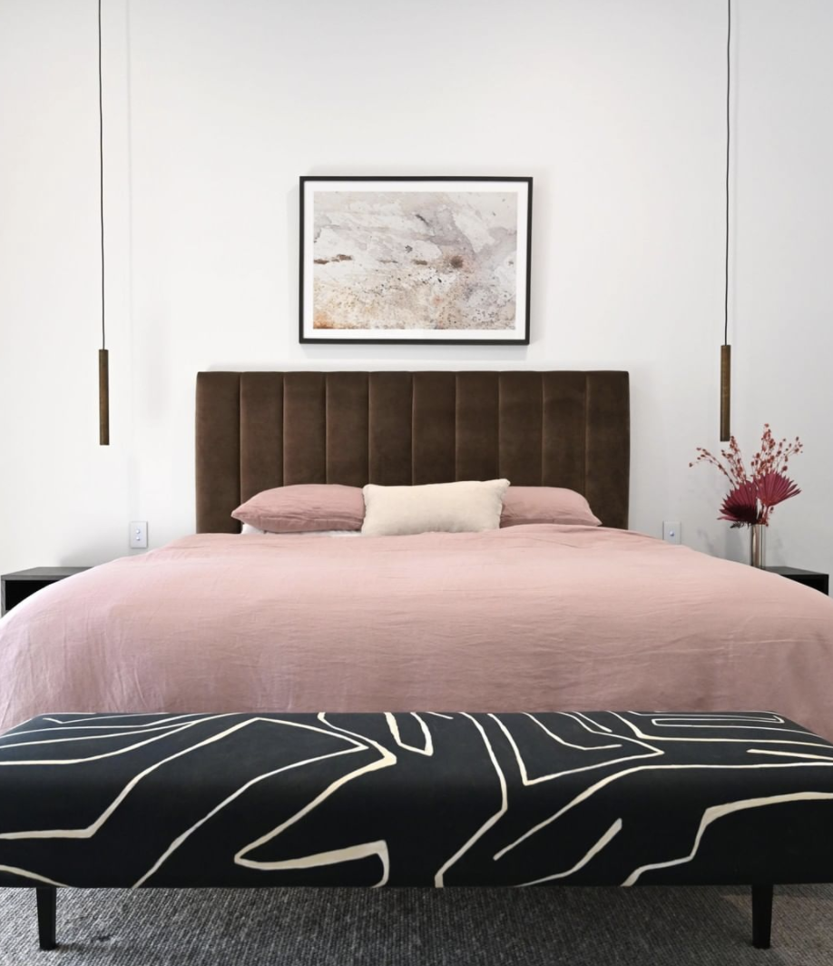 Pink bedding against a dark channelled bedhead with a patterned bench at the foot.