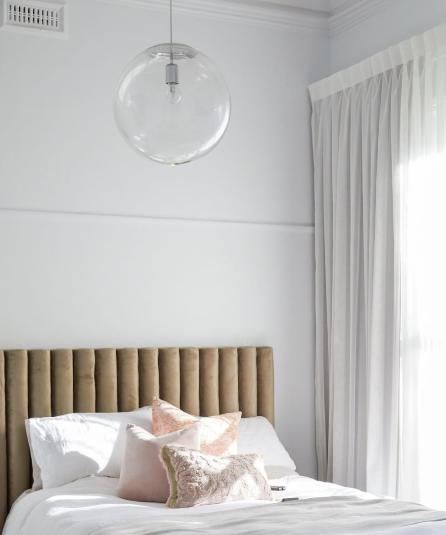 Light bedroom with a channelled tan bedhead, pale linen and a glass globe pendant.