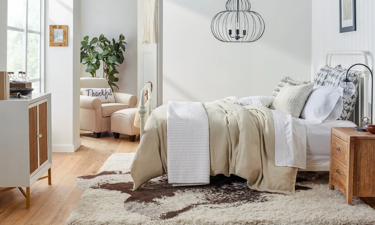 Light-filled bedroom with layered pale linen, timber furniture and a textured rug.