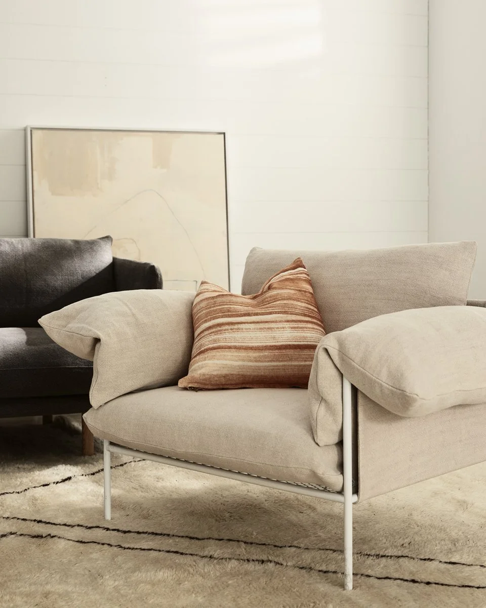 Softly upholstered pale armchair with a patterned cushion in a neutral room.