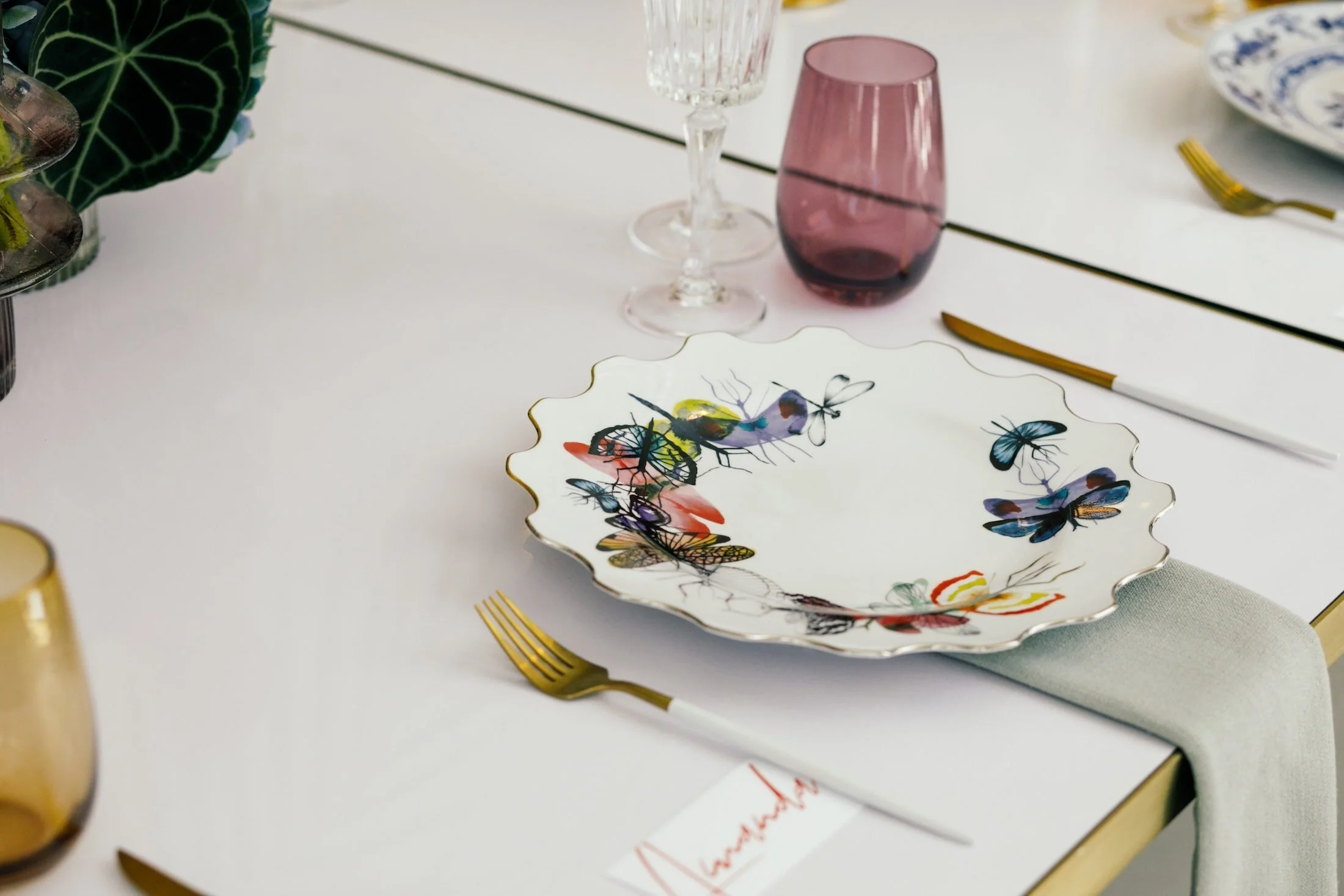 Decorative bird-patterned plate and pink drinking glass on a pale table.
