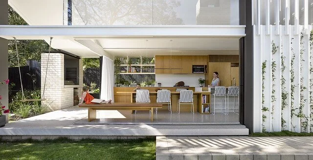 Open-plan interior connecting through wide glazing to a timber deck and garden.