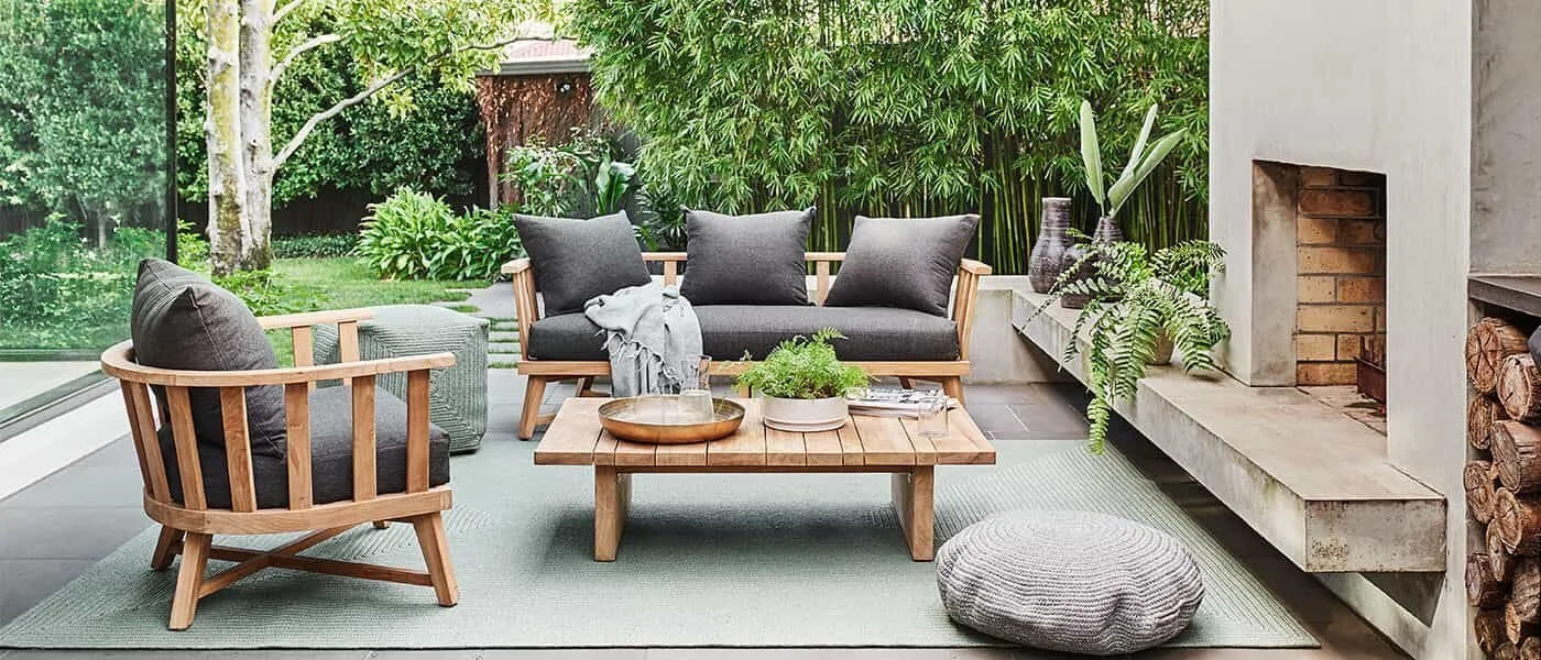 Outdoor timber seating and a low table beside a fireplace and planted garden.